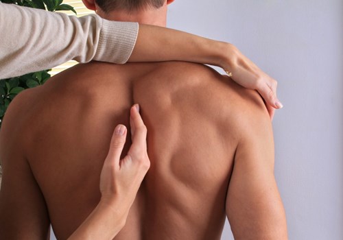A female chiropractor working on a male patients back while he stands looking away from her